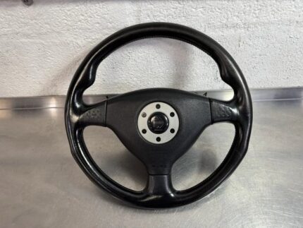 OEM Momo leather steering wheel from a JDM Mitsubishi Lancer Evolution (commonly fitted to Evo IV, V, VI, or CP9A/CT9A generations), featuring a black leather rim and a silver-accented center horn pad area with the Momo arrow logo.