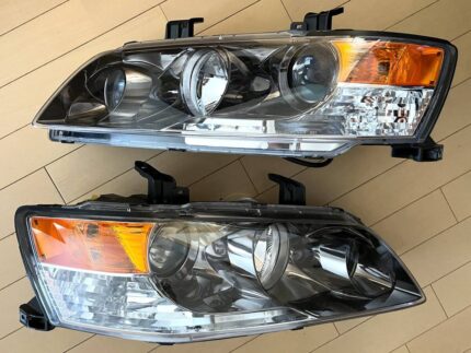 A pair of authentic Mitsubishi Lancer Evolution VIII MR / IX projector headlights and t featuring black inner housings and amber corner reflector sections and genuine Mitsubishi Lancer Evolution IX (Evo 9) JDM black chrome tail lights (OEM part numbers 8330A119 for the left and 8330A120 for the right), manufactured by Stanley.